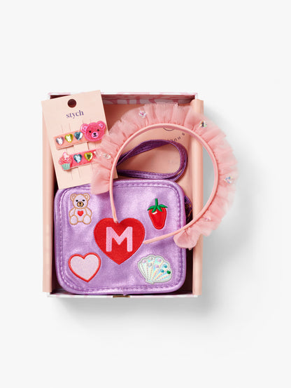 Stych Girls Pesonsalised Gift Box that included purple sparkly bag with initial and patch teddy, shell, heart appliqué, 2 Pack Teddy & Cupcake Gem Clips, Pink Ruffled Tulle & Gem Headband, packed in a pink box. 