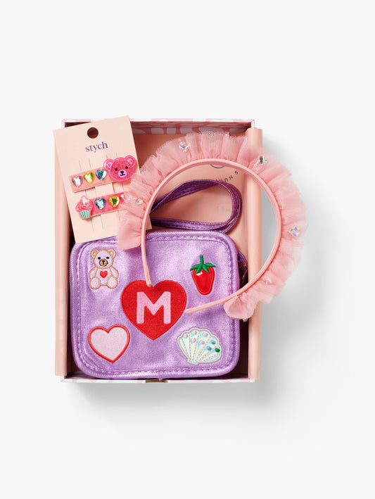 Stych Girls Pesonsalised Gift Box that included purple sparkly bag with initial and patch teddy, shell, heart appliqué, 2 Pack Teddy & Cupcake Gem Clips, Pink Ruffled Tulle & Gem Headband, packed in a pink box. 
